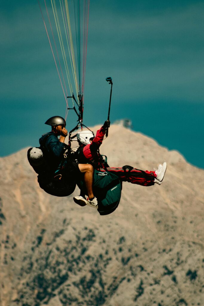 Two people enjoying a tandem paragliding experience over scenic mountains.